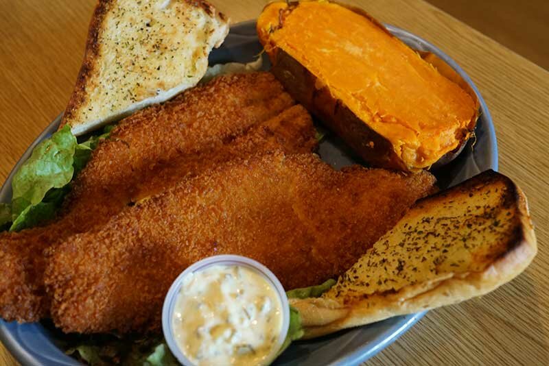 Fried fish with side of garlic bread, coleslaw and baked sweet potato